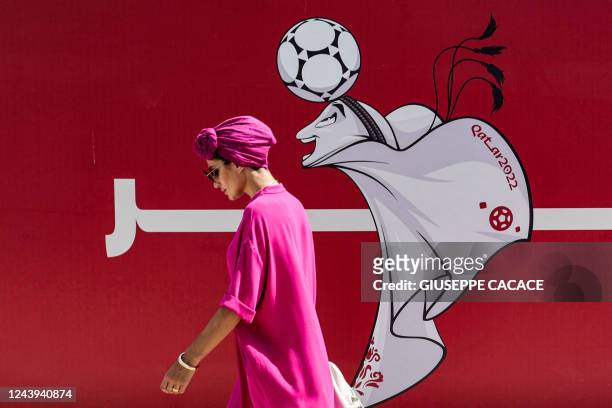 Woman walks past a construction site fence showing an illustration of the Qatar 2022 FIFA World Cup mascot "La'eeb" in West Bay in Qatar's capital...