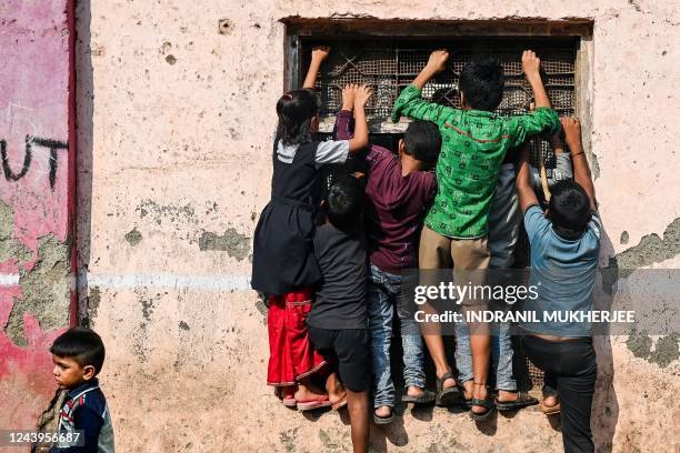 Children climb up onto the windows of a school building to catch a glimpse of a performance by artists dressed as cartoon characters inside the...