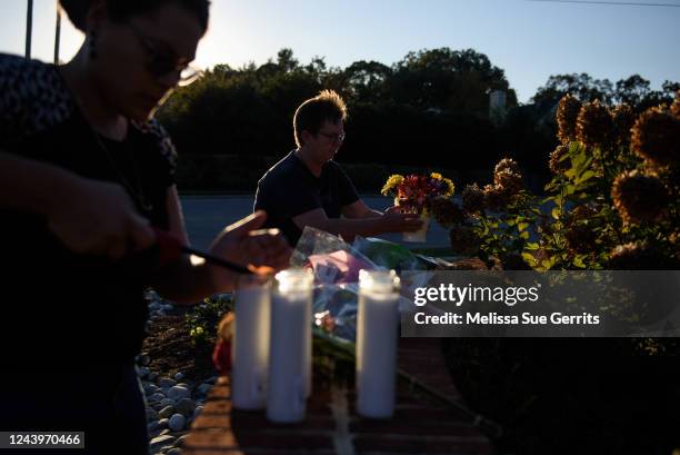 Woman lays flowers while another lights candles at the entrance of Hedingham neighborhood on October 14, 2022 in Raleigh, North Carolina. 5 candles...