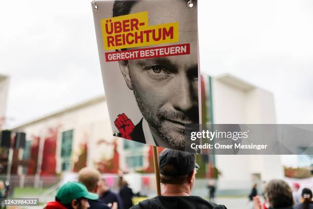 Participant holds a banner depicting German Finance Minister Christian Lindner that reads "Properly tax over-wealth", as people gather under the...