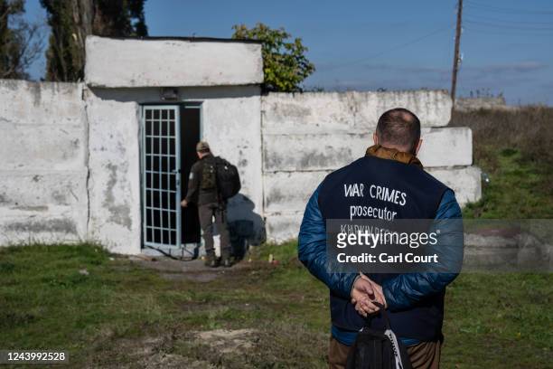 War crimes prosecutor looks on as a police officer enters an underground air raid shelter that was believed to be used as a prison by Russian...