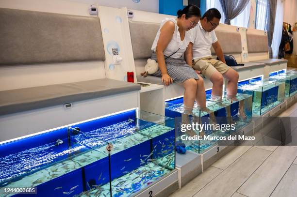 Couple of Asian tourists enjoying a fish pedicure, also known as a fish spa treatment, where customers place their feet in a tub of water filled with...