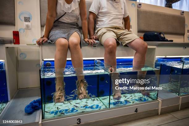 Couple of Asian tourists enjoying a fish pedicure, also known as a fish spa treatment, where customers place their feet in a tub of water filled with...