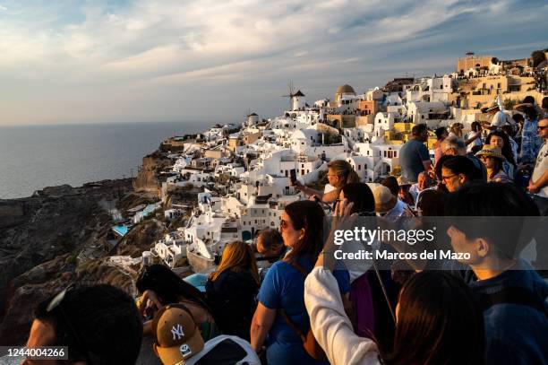 Tourists taking pictures and selfies during sunset in the town of Oia with its limewashed houses and windmills. Santorini is one of the Cyclades...