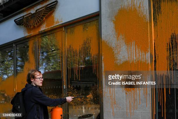 Member of the environmental activist group Just Stop Oil sprays orange paint on the window shop of the Aston Martin car show room, in central London,...