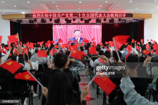 This photo taken on October 16, 2022 shows people waving national flags and Communist Party flags as they watch the opening session of the 20th...