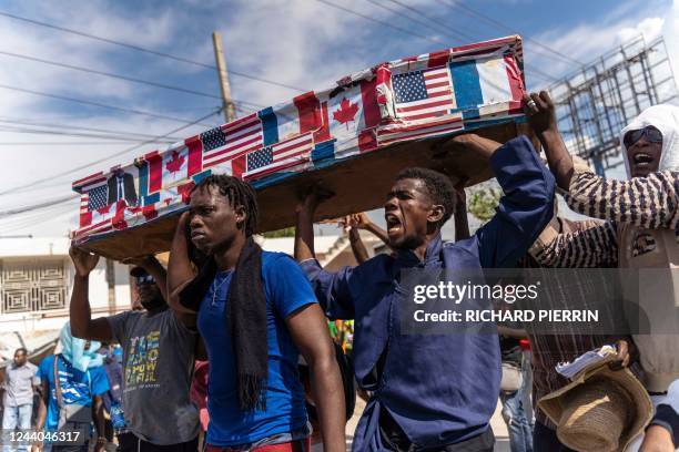 Demonstrators carry a coffin covered with American, Canadian and French flags and pictures of politicians as they protest on Jean-Jacques Dessalines...