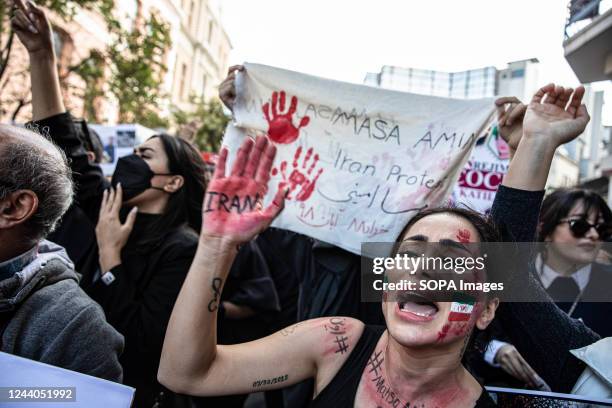 Protester with the Iranian flag painted on her face raises her red painted hand with the word Iran outside the Iranian Consulate in Istanbul during a...