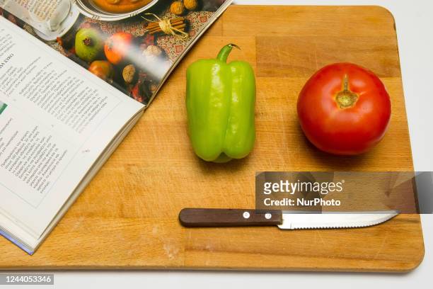 Cooking magazine, a tomato, a pepper and a knife on a wooden cutting board in Athens, Greece on October 18, 2022.