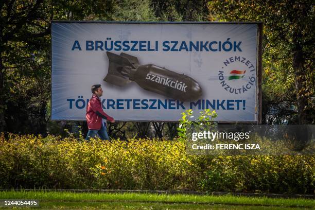 Man passes by a poster depicting a bomb reading "We are being punished by the Brussels sanctions", in Budapest on October 18, 2022. - Hungary on...