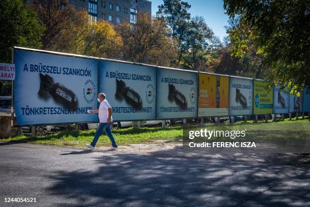 Man passes by posters depicting a bomb reading "We are being punished by the Brussels sanctions", in Budapest on October 18, 2022. - Hungary on...