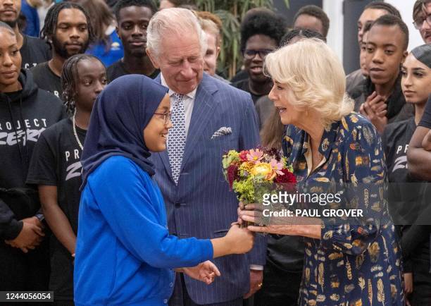 Britain's Camilla, Queen Consort , flanked by Britain's King Charles III , received a flower bouquet as she arrives to meet with members and staff of...