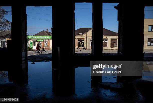 Woman cycles past a the remains of a building believed to have been used by Russian occupying forces to torture local residents, on October 18, 2022...