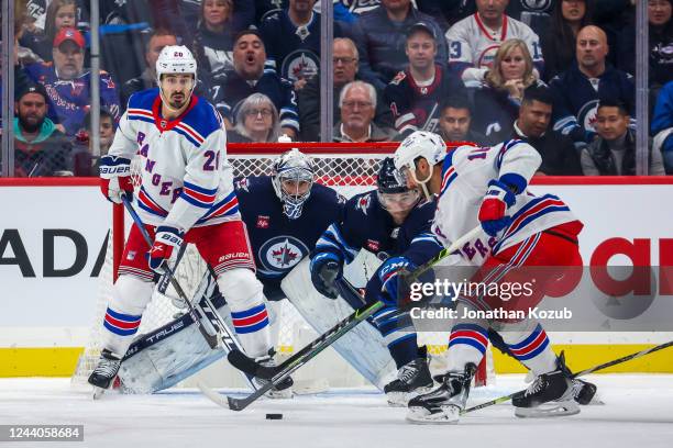 Chris Kreider of the New York Rangers looks on as teammate Vincent Trocheck plays the puck in front of goaltender Connor Hellebuyck and Neal Pionk of...