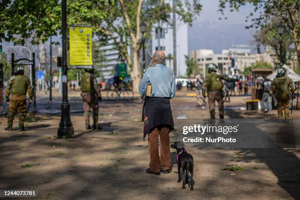 An elderly person observes the actions of the police while holding a book and accompanied by his dog in Santiago de Chile on October 18, 2022. During...