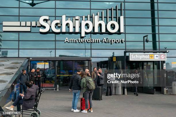 Schiphol Amsterdam Airport logo as seen on the glass surface over the main entrance of the airport while passengers are around. Passengers are seen...