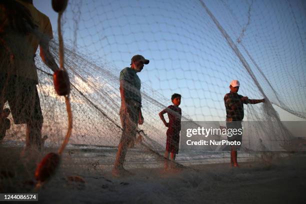 Palestinian fishermen pulling their net along a beach in Gaza City at sunset, on October 19, 2022.