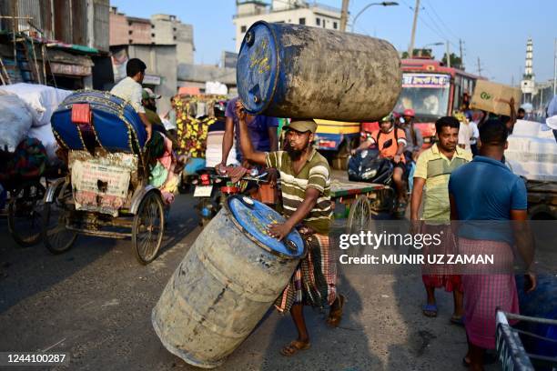 Labourer transports plastic drums along a busy street in Dhaka on October 20, 2022.