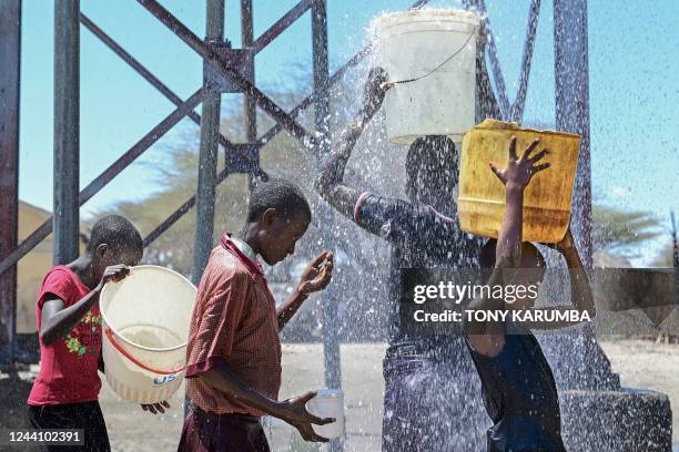 Young girls from the pastoral Turkana community stand on October 18, 2022 under an overflowing water storage tank to fill their containers at a local...