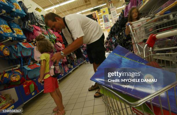 Child tries a backpack as she and her father look at back-to-school supplies in a supermarket in Rots, western France, 20 July 2006. Une petite-fille...