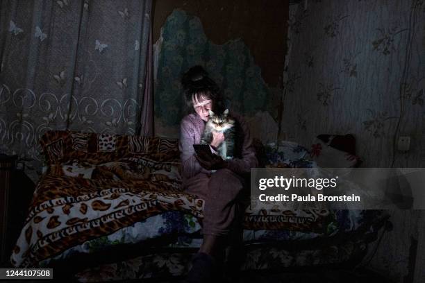 Tetyana Safonova sits with her cat Asya as she looks at her mobile phone during a power outage on October 20, 2022 in Borodyanka, Ukraine. Tetyana...