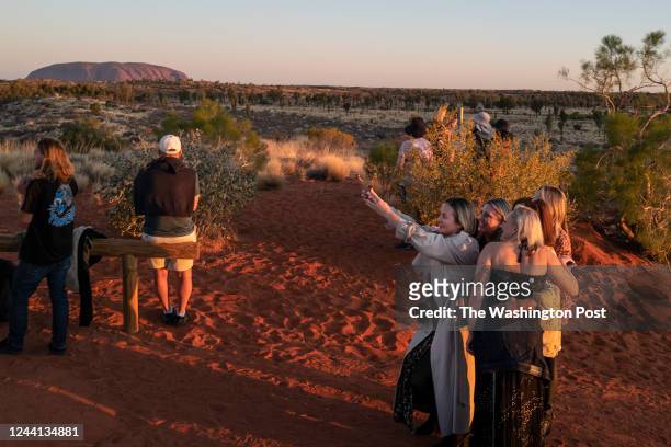 Tourists, including some dressed up for a night out taking a selfie, watch the sun set on Uluru, formerly known as Ayers Rock, a monolith that rises...