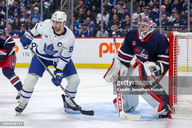 John Tavares of the Toronto Maple Leafs and goaltender Connor Hellebuyck of the Winnipeg Jets keep an eye on the play during first period action at...