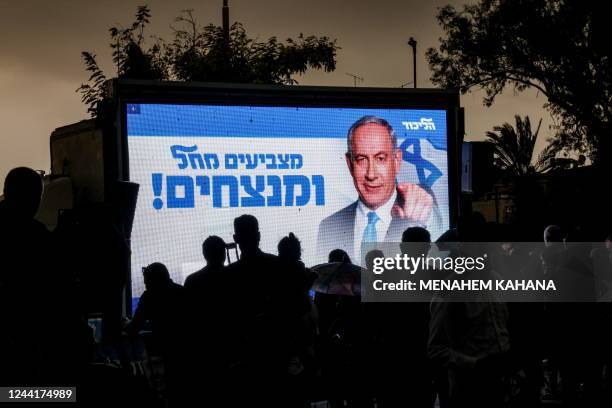 People stand before a screen showing Israeli Likud party leader and former prime minister Benjamin Netanyahu next to the campaign tag-line "vote...