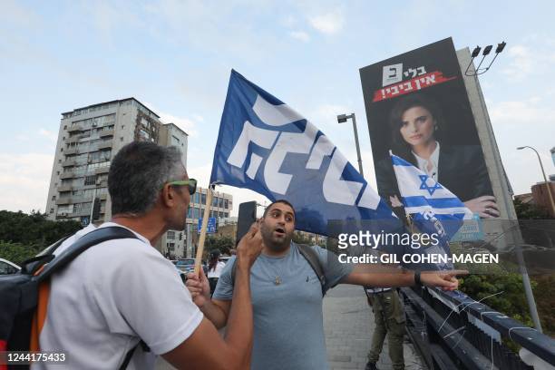 Likud supporters wave party and national flags on a bridge overlooking a highway, near a poster of Israeli Minister of Interior and Jewish Home party...