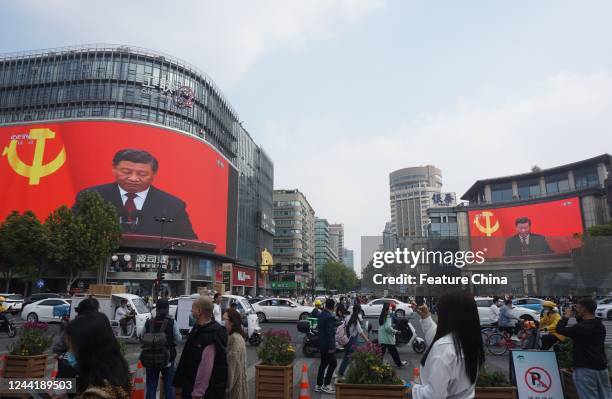 People pass a crossing where a giant screen televising a speech by Xi Jinping at closing ceremony of the 20th National Congress of the Communist...