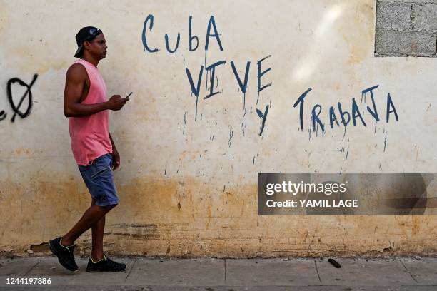 Man passes by a graffiti that reads "Cuba lives and works" in Havana, on October 24, 2022.