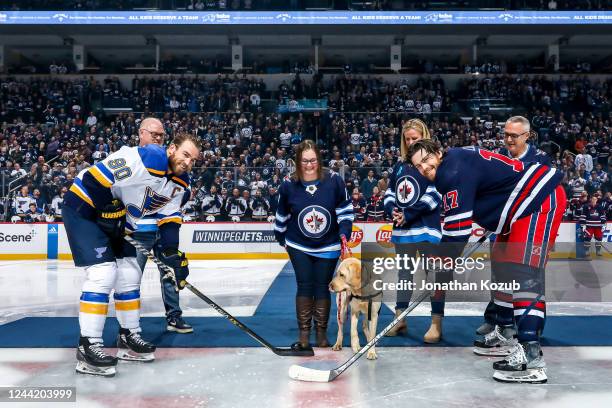 Ryan O'Reilly of the St. Louis Blues and Adam Lowry of the Winnipeg Jets take part in the ceremonial puck drop with Toba Centre facility dog, Duke,...