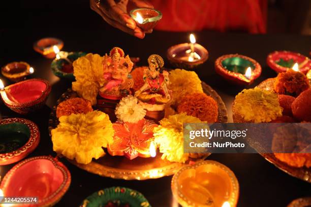 Hindu devotee places diyas by idols of Lord Ganesh and Goddess Laxmi alongside a tray of ladoos during the festival of Diwali at a Hindu temple in...