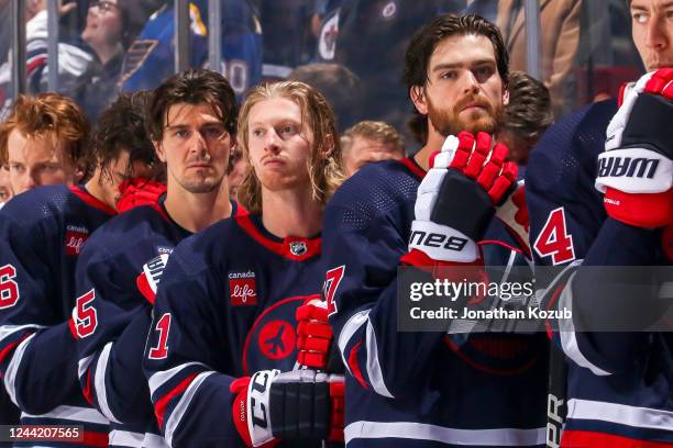 Mark Scheifele, Kyle Connor and Adam Lowry of the Winnipeg Jets look on from the bench during the singing of the National anthems prior to puck drop...
