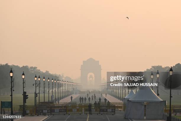 People walk along a road near India Gate amid smoggy conditions in New Delhi on October 25, 2022. - New Delhi woke up to toxic smog on October 25...