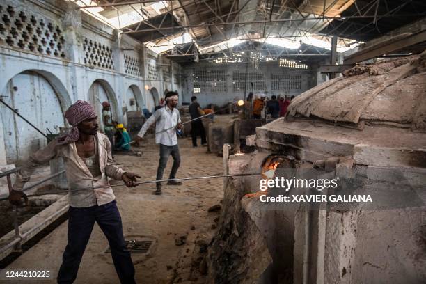 In this picture taken on October 12 workers use metal rods to collect molten glass from a furnace during the manufacturing process of glass bangles...