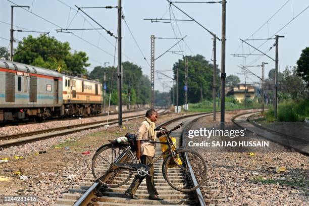 Man carries his bicycle while crossing a railway track in New Delhi on October 26, 2022.