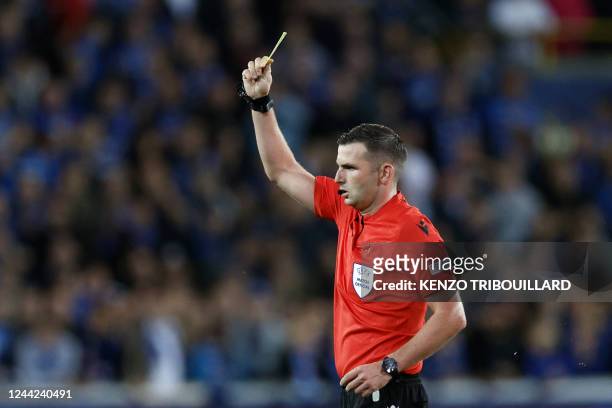 English referee Michael Oliver show a yellow card to Club Brugge's Ghanaian defender Denis Odoi during the UEFA Champions League Group B second leg...