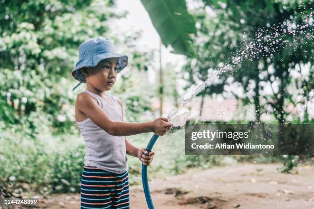a boy playing spraying water in the backyard - kids fun indonesia stock pictures, royalty-free photos & images