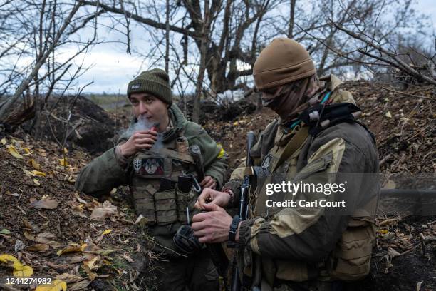 Ukrainian soldier of Russian descent loads bullets into a magazine as another smokes a vaping pen in a trench around 150 metres from a Russian...