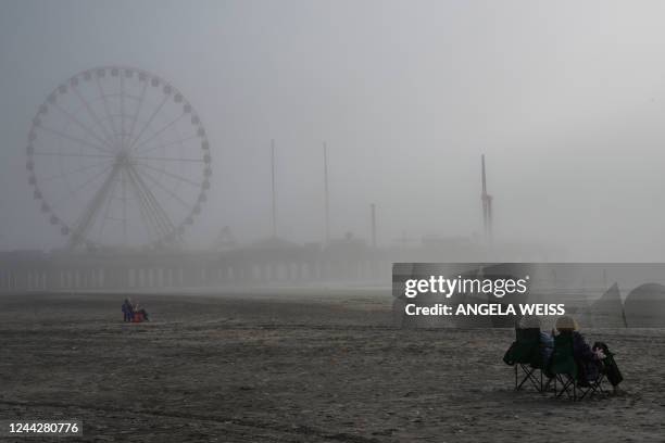 People sit on the beach near Steel Pier on a foggy morning in Atlantic City, New Jersey on October, 2022. - Ten years after the devastating hurricane...