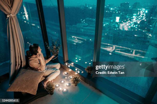 an asian chinese teenager girl enjoying music in a rainy day at her apartment corner listening to music with headphone songs from her smart phone - girl rain night stock pictures, royalty-free photos & images