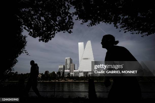 Passers-by are silhouetted as they walk along the banks of river Rhine next to the Roche towers, designed by architects Herzog and de Meuron, the...