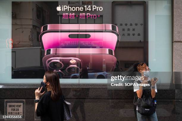 Pedestrian using a smartphone walks past an American multinational technology company, Apple iPhone 14 Pro advertisement in Hong Kong.