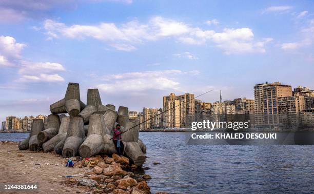 Man uses fishing rod while standing next to the concrete blocks installed along the harbour waterfront to break the Mediterranean sea waves in...