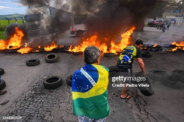 Demonstrator wearing a Brazilian flag looks at a person putting tyres to make a burning barricade as truck drivers and supporters of President Jair...