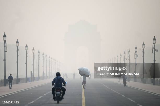 Man carries a sack along the road in front of India Gate amid smoggy conditions in New Delhi on November 1, 2022.