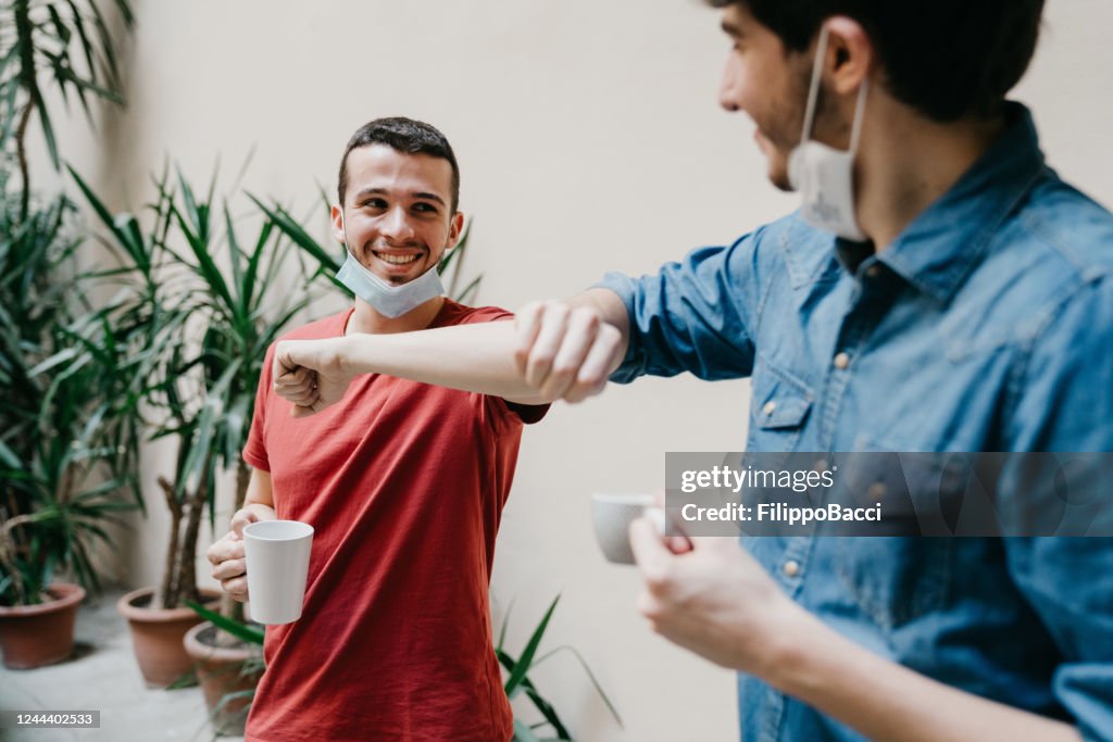 Two colleagues greeting each other with an elbow bump during a coffee break