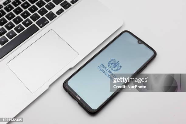 In this photo illustration a World Health Organization logo seen displayed on a smartphone screen on a desk next to a Macbook in Athens, Greece on...