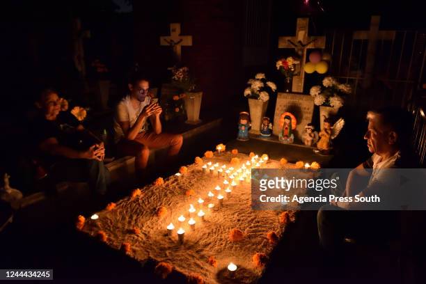 Visitors sit around a grave with flowers and candles during 'Day of the Dead' celebrations at Colima Municipal cemetery on November 1, 2022 in...